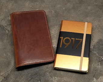 May include: A brown leather journal and a gold journal with a black band and the number 1917 printed in gold.