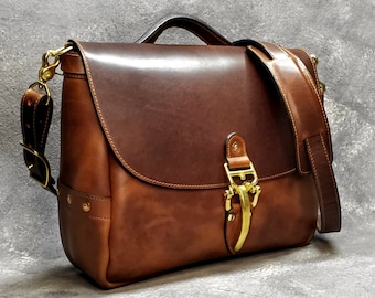 May include: A brown leather satchel bag with a brass buckle and a long adjustable strap. The bag has a flap closure and a top handle.