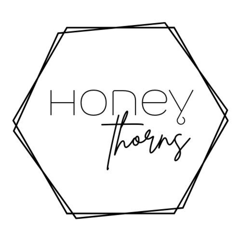 May include: A black and white logo featuring the words "HONEY thorns" inside a geometric hexagon shape. The word "HONEY" is in a sans-serif font, while "thorns" is in a cursive script.