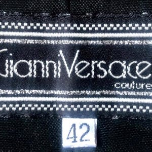 May include: A black label with the text "Gianni Versace couture" in white. The label is rectangular with a white border and a small white tag with the number "42".
