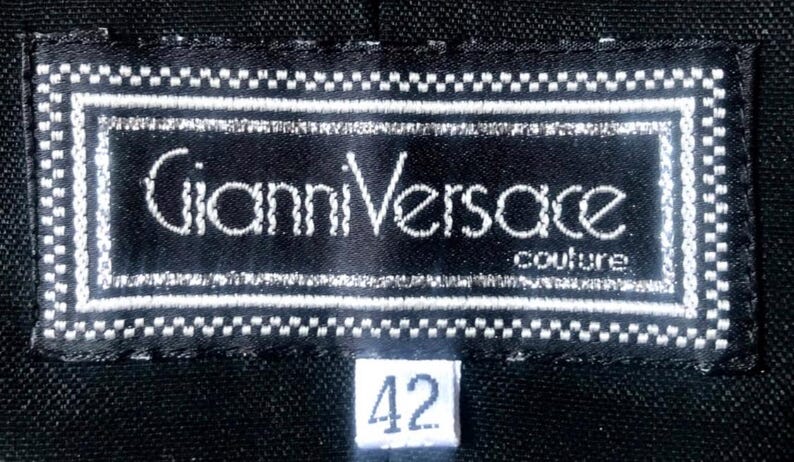 May include: A black label with the text "Gianni Versace couture" in white. The label is rectangular with a white border and a small white tag with the number "42".