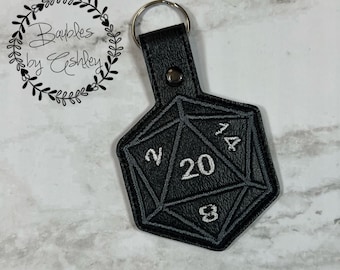 May include: Black leather keychain shaped like a twenty-sided die with white stitching and numbers. The keychain has a silver metal ring.