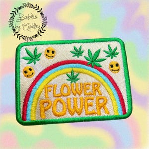 May include: Embroidered patch with a green border, featuring a rainbow, cannabis leaves, and smiley faces. The words "FLOWER POWER" are in yellow. The patch is rectangular.
