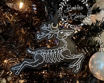 Può includere: Ciondolo a forma di renna in feltro nero con dettagli scheletrici ricamati in bianco. Il ciondolo è appeso a un albero di Natale nero. Il ciondolo ha un anello per appenderlo e il testo "Bubles by Eshley" è visibile sullo sfondo.