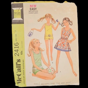 Może przedstawiać: Vintage wzór krawiecki McCall's 2416 na stroje kąpielowe, topy i spódnice dla dziewczynek. Okładka zawiera ilustracje dziewczynek w strojach kąpielowych. Zawiera tekst "NEW EASY" i "TWO-COLOR GUIDE included in pattern".
