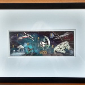 May include: A framed set of Star Wars postage stamps featuring various spaceships and characters from the movie franchise. The stamps are arranged in a horizontal row against a dark blue background with stars. The text "Star Wars" is printed in gold letters below the stamps.