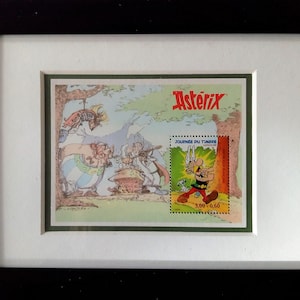 May include: A framed illustration of a comic book character, Asterix, with the text "Asterix" and "Journées du Timbre" in red and black. The illustration is surrounded by a green border.