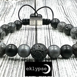 May include: A black and gray beaded bracelet with a silver clasp. The bracelet features black lava rock beads, gray gemstone beads, and black matte beads.