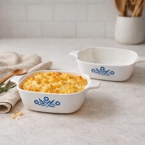 May include: Two white rectangular baking dishes with handles. One dish contains a golden-brown casserole. Both dishes have a blue floral design. The dishes are on a light-colored surface.