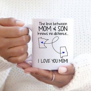 May include: White ceramic mug with a black design that reads "The love between MOM & SON knows no distance... I LOVE YOU MOM!" The design also includes a map of Minnesota and Alabama with a blue heart in each state.