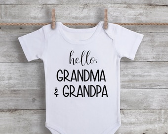 May include: White baby onesie with black text that reads "hello, grandma & grandpa".