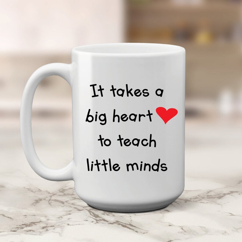 May include: White ceramic coffee mug with a black inscription that reads "It takes a big heart to teach little minds" with a red heart symbol.