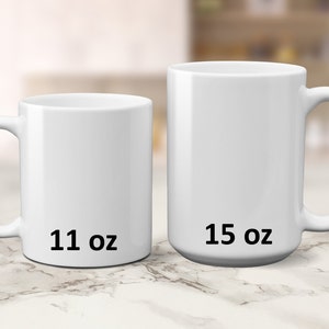 May include: Two white ceramic mugs, one 11 oz and one 15 oz, on a marble surface.