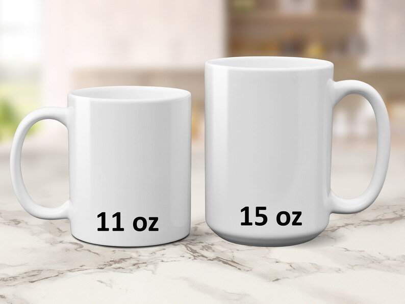 May include: Two white ceramic mugs, one 11 oz and one 15 oz, on a marble surface.