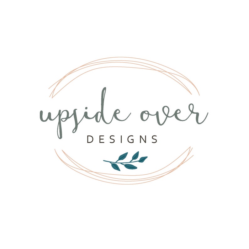 May include: A logo design featuring the text "upside over DESIGNS" in a handwritten style, enclosed within a double-lined oval. The text is in a muted teal color, with a sprig of teal leaves at the bottom. The oval is in a light brown color, all set against a white background.