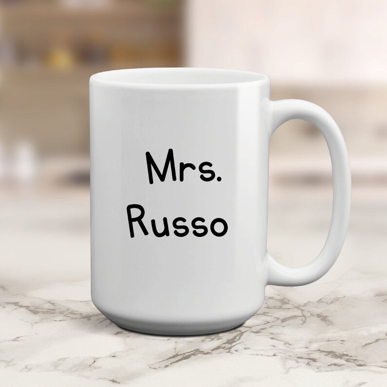 May include: White ceramic coffee mug with black text that reads "Mrs. Russo"