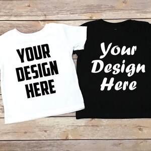 May include: Two blank t-shirts, one white and one black, laid flat on a wooden surface. Both shirts have the text "Your Design Here" printed on them.
