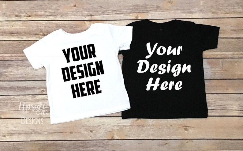 May include: Two blank t-shirts, one white and one black, laid flat on a wooden surface. Both shirts have the text "Your Design Here" printed on them.