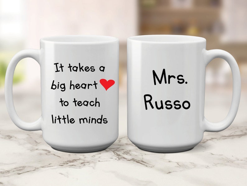 May include: Two white ceramic mugs. One mug has the text "It takes a big heart to teach little minds" with a red heart. The other mug has the text "Mrs. Russo".