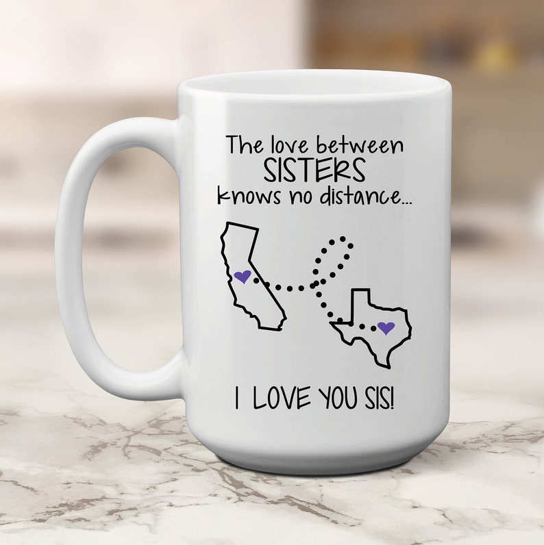 May include: White ceramic mug with a black graphic and text. The text reads "The love between SISTERS knows no distance... I LOVE YOU SIS!" The graphic shows the outline of California and Texas, connected by a dotted line.