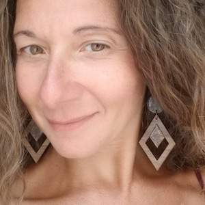 May include: A woman wearing a pair of brown and silver geometric wooden earrings. The earrings are shaped like a diamond with a smaller diamond inside.