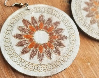 May include: A pair of large, round wooden earrings with a white background and a brown and orange floral design. The earrings have silver hooks.