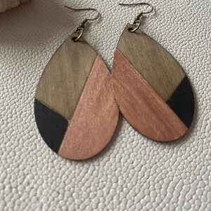 A pair of teardrop-shaped earrings lightweight wood earrings with a geometric block design. The earrings are made of thin wood and have a black, walnut stain and rose gold finish sections.