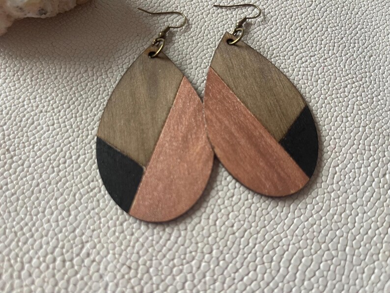 A pair of teardrop-shaped earrings lightweight wood earrings with a geometric block design. The earrings are made of thin wood and have a black, walnut stain and rose gold finish sections.