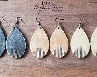 May include: Three pairs of teardrop-shaped wooden earrings with a geometric design. The earrings are in three colours: grey, beige, and cream.