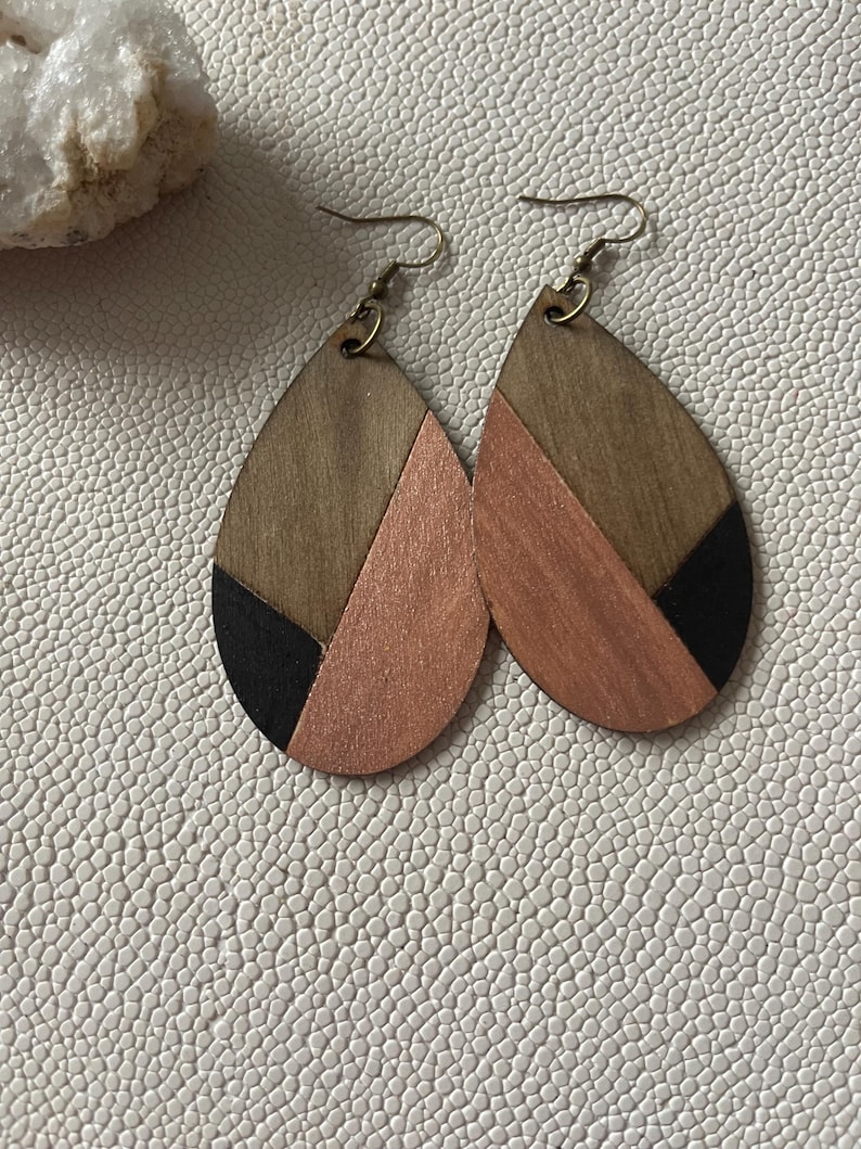 A pair of teardrop-shaped earrings lightweight wood earrings with a geometric block design. The earrings are made of thin wood and have a black, walnut stain and rose gold finish sections.