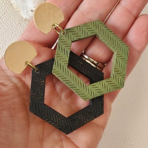 May include: A pair of geometric earrings with a black and green wood design. The earrings are made of two hexagonal shapes, one inside the other. The larger hexagon is green and the smaller hexagon is black. The earrings are attached to gold-coloured hooks.
