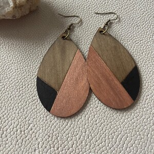 A pair of teardrop-shaped earrings lightweight wood earrings with a geometric block design. The earrings are made of thin wood and have a black, walnut stain and rose gold finish sections.