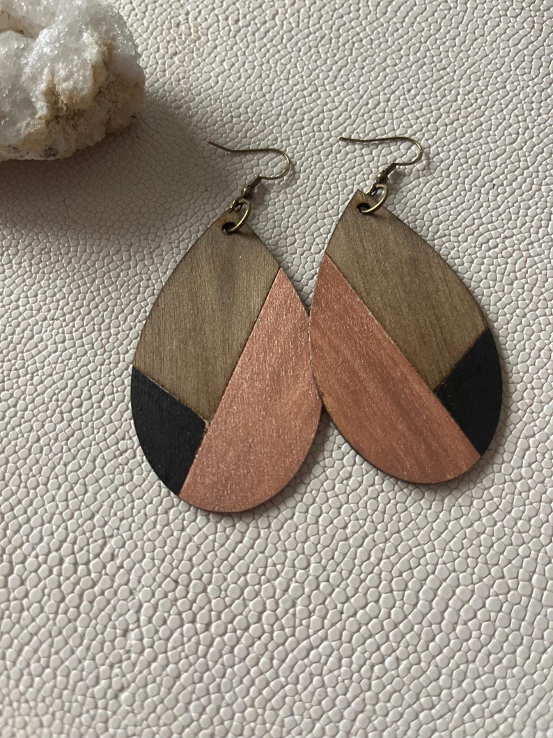 A pair of teardrop-shaped earrings lightweight wood earrings with a geometric block design. The earrings are made of thin wood and have a black, walnut stain and rose gold finish sections.