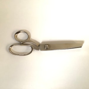 May include: A pair of large, shiny, silver-colored scissors. The scissors have two finger holes and a long, straight blade. The blades are held together with a silver rivet. The scissors are designed for cutting fabric or other materials.