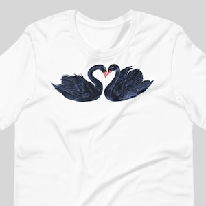 May include: A white t-shirt with a black and white illustration of two black swans with their necks intertwined in a heart shape.