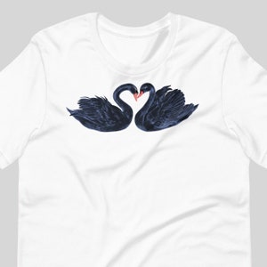 May include: A white t-shirt with a black and blue illustration of two black swans with their necks intertwined in a heart shape.