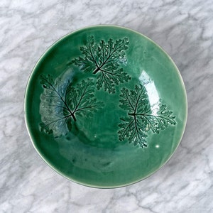 May include: A green ceramic bowl with a fern leaf design. The bowl is round and has a slight lip.