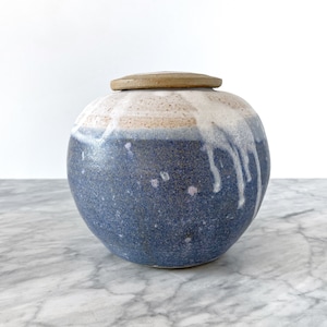 May include: A blue and white ceramic jar with a lid. The jar has a speckled blue glaze with white drips and a white band around the top. The lid is a light brown color.