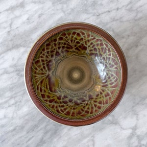 May include: A brown ceramic bowl with a green and brown glaze. The glaze has a swirling pattern.