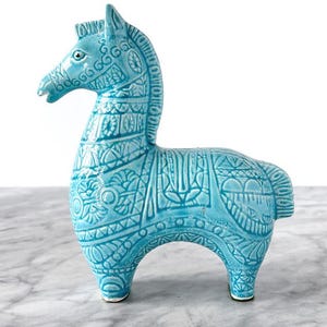 Może przedstawiać: Turkusowa ceramiczna figurka konia ze skomplikowanymi wytłoczonymi wzorami. Koń ma szczegółową grzywę, ogon i ciało i stoi na czterech nogach. Figurka jest przedmiotem dekoracyjnym.