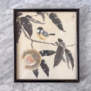 May include: A framed watercolor painting featuring a small bird perched on a branch with leaves and a chestnut. The bird has a black head, yellow chest, and gray wings. The painting is in a black bamboo-style frame.