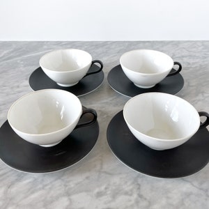 May include: Set of four white teacups with black saucers. The cups and saucers have a simple, modern design.