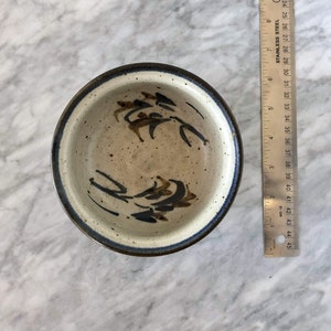 May include: A small, white ceramic bowl with a blue and brown design. The bowl has a speckled glaze and a dark blue rim.
