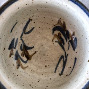 May include: A white ceramic bowl with a blue rim and brown and blue floral designs. The bowl is speckled with brown spots.
