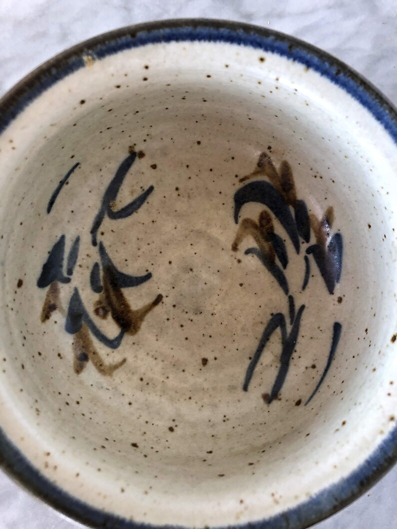 May include: A white ceramic bowl with a blue rim and brown and blue floral designs. The bowl is speckled with brown spots.