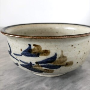 May include: A small, white ceramic bowl with a brown rim and blue and brown floral designs.