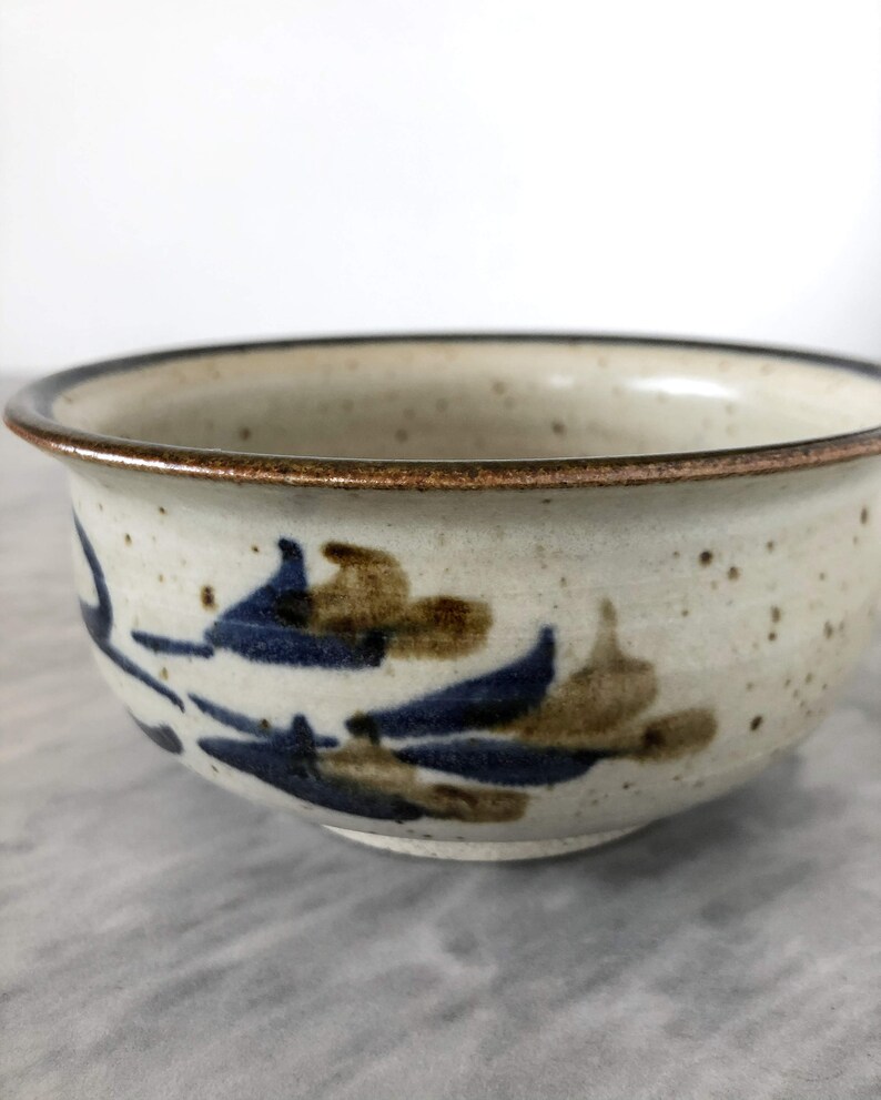 May include: A small, white ceramic bowl with a brown rim and blue and brown floral designs.