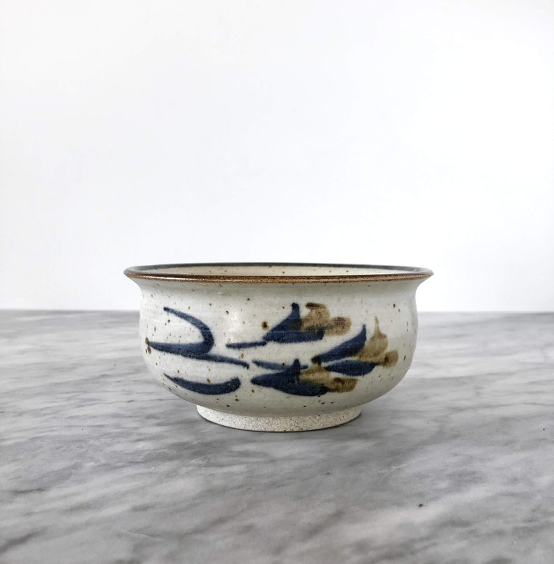 May include: A white ceramic bowl with a brown rim and blue and brown floral design.