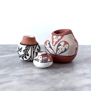 May include: Three small, hand-painted pottery vases with geometric designs in black, white, and red. The vases are on a white marble surface.