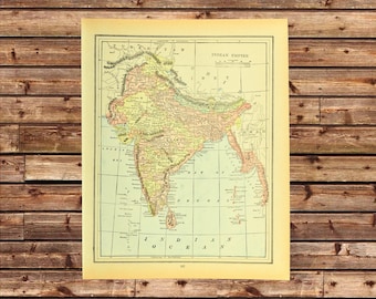 May include: A vintage map of the Indian Empire, featuring detailed geographical information. The map is printed on aged paper with a cream-colored border. The map includes text labels and is set against a wooden background.